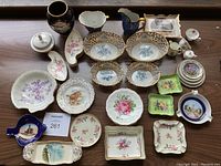 Collection of small vintage floral dishes including plates, bowls, trays, ashtrays, and vase, arranged on a wooden surface.