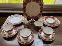 Full arrangement of English tea set items including cups, saucers, plates, creamer, and sugar bowl all featuring pink cabbage rose floral patterns with gold trim