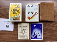 Two decks of cards shown including a vintage Gypsy Witch Fortune Telling deck with instruction booklet and a Rider Tarot Deck Pocket Edition box, with a card showing 4 of clubs and red key symbol from the Gypsy Witch deck.