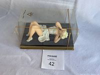 Photo showing side view of figurine inside clear display box with gold trim, resting on black base.