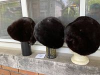 Three black mink hats displayed side by side on stands
