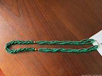 Full view of entire malachite necklace laid flat on wood surface showing length and bead consistency.