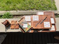 Overview showing charcuterie boards stacked and teak coasters with holder beside them outdoors.