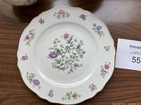 Top view of scalloped dinner plate decorated with pastel multicolor flowers and gold rim