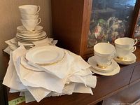White and gold Royal Albert dishes including stacked plates and cups alongside Royal Doulton cups and saucers.