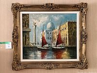 Full frontal view of framed oil painting showing two red-sailed boats in canal with domed building in background
