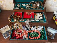 Wide view of the jewelry lot showing copper bracelets on top, assorted brooches, rhinestone pieces, beaded necklaces in multiple colors, and cufflinks in boxes.