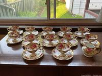 Wide view of 12 cups and saucers with matching creamer jug on wooden surface