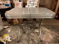 Side view of vintage kitchen table showing the full rectangular grey arborite top with split center and chrome legs in industrial space.