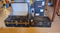 Three antique steamer trunks stacked in basement showing top open trunks and closed lower trunk