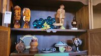 Shelf with pottery mushroom-shaped covered piece, candleholder, pottery goblet signed Jacob, wood carved sculptures and glass grapes.