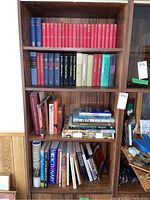 Shelf containing assorted hardcover and paperback books, including red, blue, black, cream, and green spines. Titles by notable authors visible.