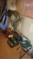 Lot contents showing fishing nets, tackle boxes with fishing lures, two fishing rods leaning against the basement wall, and a collapsible green stool.