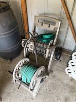 Two plastic hose caddies, one on wheels, with garden hoses wrapped around, and two additional hoses stacked on one caddy