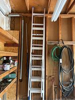 Photo showing the two ladders side by side hanging on a wall in a garage or workshop. One is white wooden step ladder; the other is an aluminum multi-section extension ladder.
