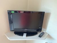 Front view of a Samsung 21-inch flat-screen TV on a white corner shelf with remote control beside it.
