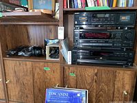 Full view of the audio equipment stack on a wooden cabinet including cassette deck, receiver, CD player, headphones, and cables