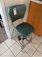 Angle view showing teal vinyl seat and backrest with patterned design and metal frame