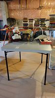 Front view of the utility table showing white plastic top and black collapsible legs in a basement.