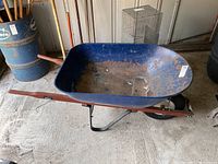 Full side view of the metal wheelbarrow showing blue basin, wood handles, and single wheel.