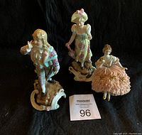 Three porcelain figurines including Victorian Lace Lady, man in blue coat, and lady with pink umbrella, all standing on decorative bases.