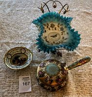 Overall lot showing the blue glass brides basket with ruffled edges and ornate handle, the hand painted ashes pot with handle decorated in pastel and gold, and the small hand painted dish with floral and gold border.