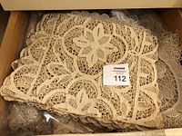 Drawer full of neatly stacked and bagged antique table linens showing layered bone and ivory lace doilies and runners