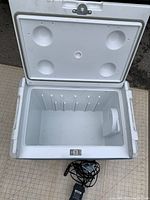 Open view of cooler showing white interior with molded ribs and built-in compartment, lid interior with cup holders, and power cords.