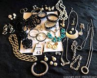 Full lot photo showing a collection of costume jewellery including necklaces, bracelets, earrings, and brooches placed on a black backdrop.