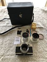 Full lot with Kodak camera body, two Schneider-Kreuznach lenses, black carrying case, and some paperwork on a beige cloth surface