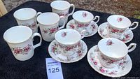 Overview of 4 bone china tea cups with matching saucers and 4 coffee mugs with floral lavender rose pattern and gold trim.