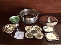 Full group of silver plate and silver filled items on wooden surface including bowl with lid, divided dish, footed bowl, small trays.