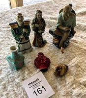 Lot contents of six items including four figurines and two small vases arranged on fabric surface.