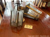 Two vintage hanging lamps of different styles on wood table, showing metal frames and glass panels