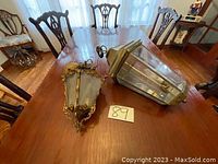 Photo showing two lamps placed on a wooden dining table, one is an ornate metal and glass lantern style lamp, the other an antique style wall sconce with frosted glass.