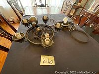 Photo showing two dark metal antique chandeliers placed on a dining table, showing their multiple light sockets and hanging chains.