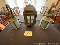 Front view of three antique hanging lanterns on table, showing metal frame, glass panels, hanging handles, condition and structure.