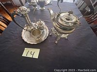 Full view of antique silver tea set on dark tablecloth including teapot, platter, sugar and creamer pots