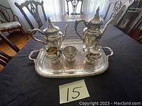 Full view of the antique silver tea set on a black tablecloth, showing the teapot, coffee pot, creamer, sugar bowl, waste bowl, and a large rectangular serving tray with handles.