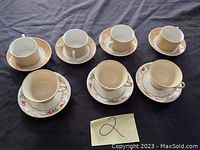 Four sets of tea cups with saucers on a dark fabric background, showing two plain white cups and two with floral pattern.