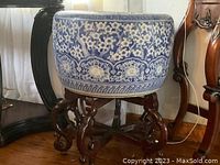 Full view of the blue and white floral ceramic pot standing on the wooden stand, showing the overall size and style