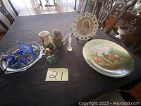 Photo of all items including blue glass flowers, silver-tone tray, deer plate on stand, floral candle, green candle holder with candle, religious plate on stand.