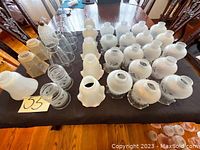 Overview photo of multiple glass lamp shades arranged on a table, showcasing variety of shapes, sizes, and styles in clear and frosted glass.