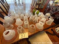 Several vintage glass lamp shades arranged on a wooden table showing various styles including frosted, clear, embossed, and ribbed glass finishes, some with metal fitting rings (brass/copper). Sizes appear to range from 4 to 10 inches approximately.