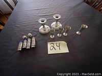 Photo showing two sterling silver candle holders, three small silver cups, and three glass salt shakers with silver lattice tops on a black table.