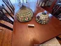 Two Tiffany style stained glass lamp shades on a wooden dining table showing a larger and smaller shade side by side.