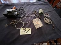 Photo showing the entire lot of items: antique video camera, wire tap telegraph, small green bell, two old padlocks and chain on black cloth background.