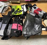 7 bags arranged on wood surface, including leather work bags and colorful sling bags