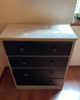 Front view of vintage dresser showing four black drawers with various knobs and light painted top with visible scratches