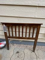 Wood twin size headboard standing against exterior house siding with installation hardware attached.